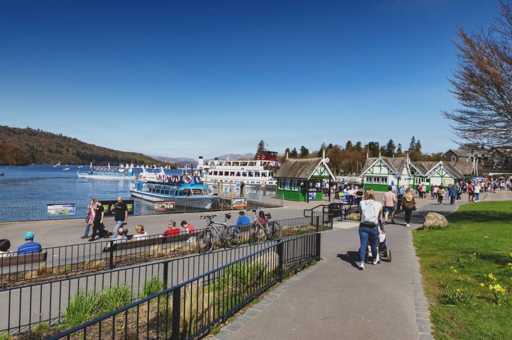 People walking along the waterfront in Bowness-on-Windermere with a boat on the lake