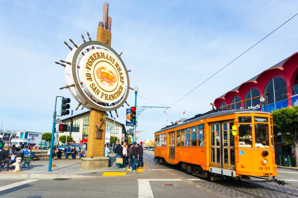 Fisherman’s Wharf sign beside an orange tram and waterfront buildings