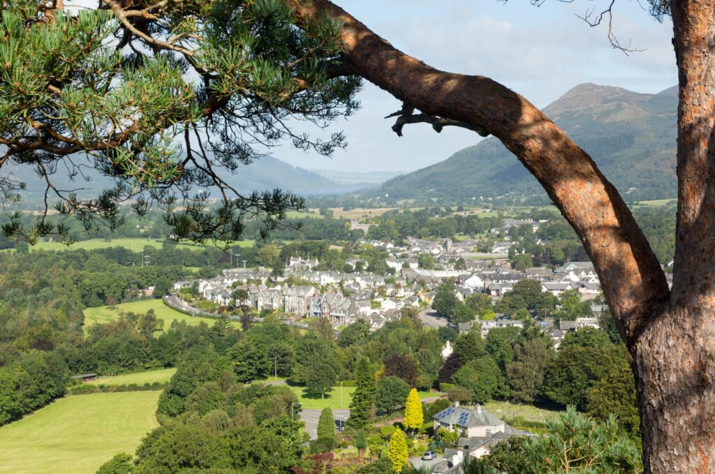 View of Keswick from a wooded hillside with green fields and mountains beyond