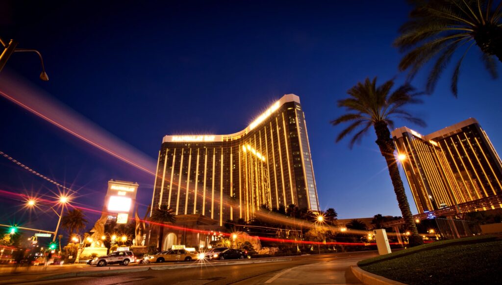 Illuminated Mandalay Bay tower with palm trees and passing traffic at night