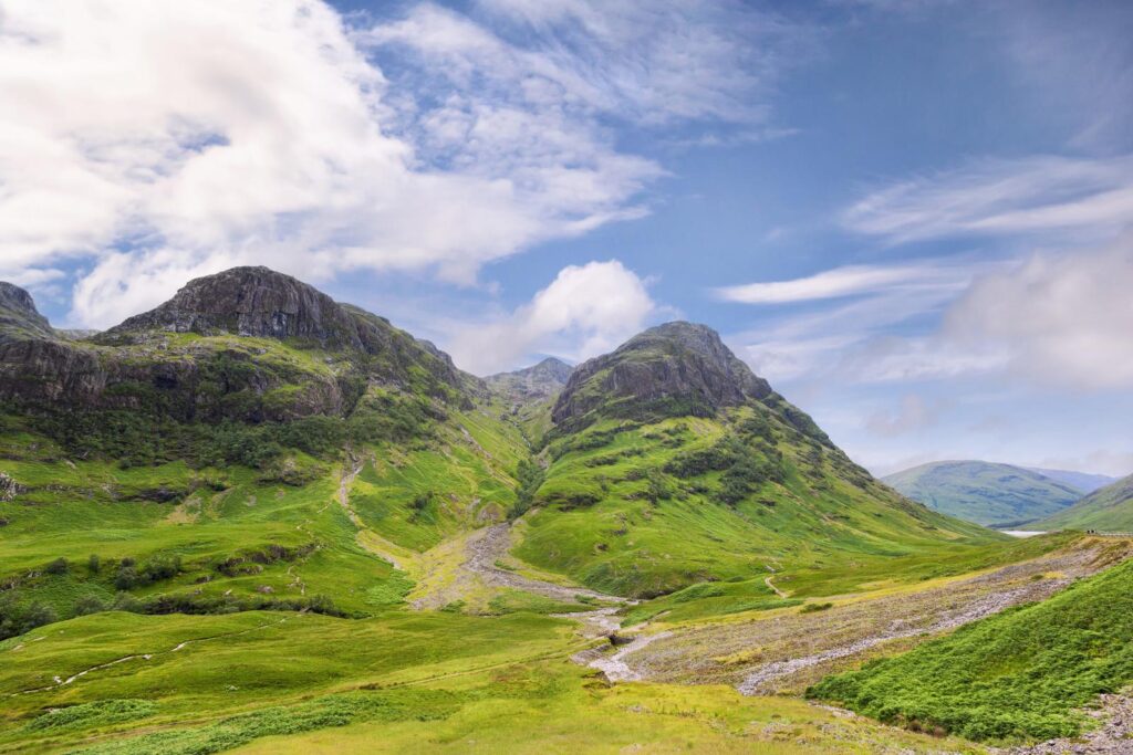 Green mountain slopes and a road in the valley beneath the Three Sisters of Glencoe