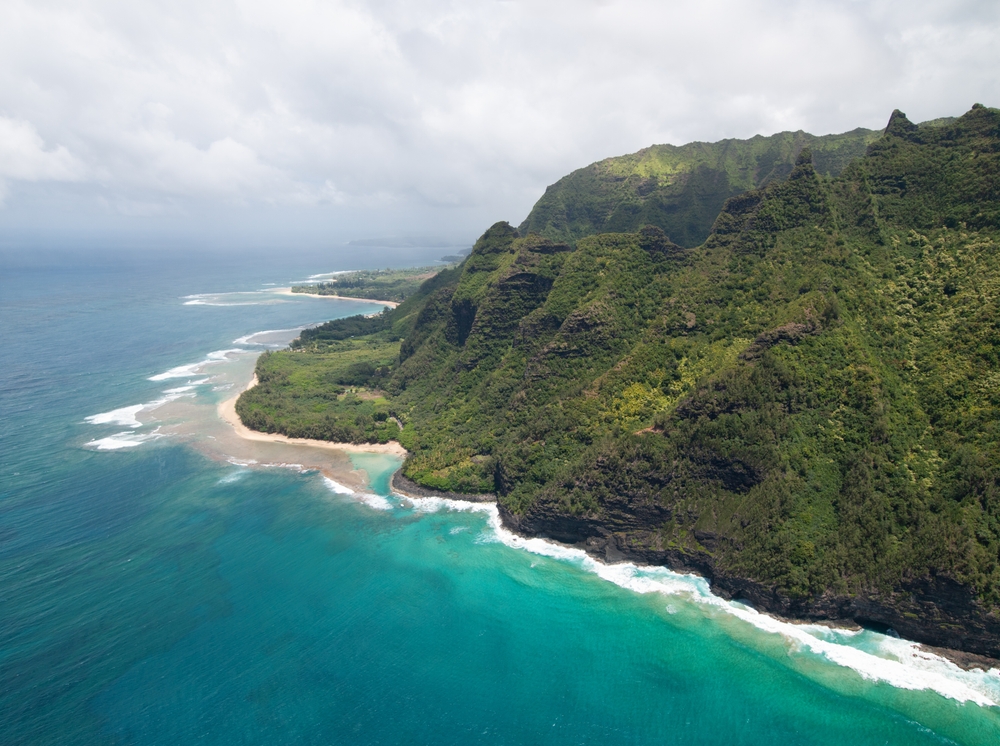 Aerial view of the Na Pali Coast on Kauai with steep green cliffs and turquoise sea