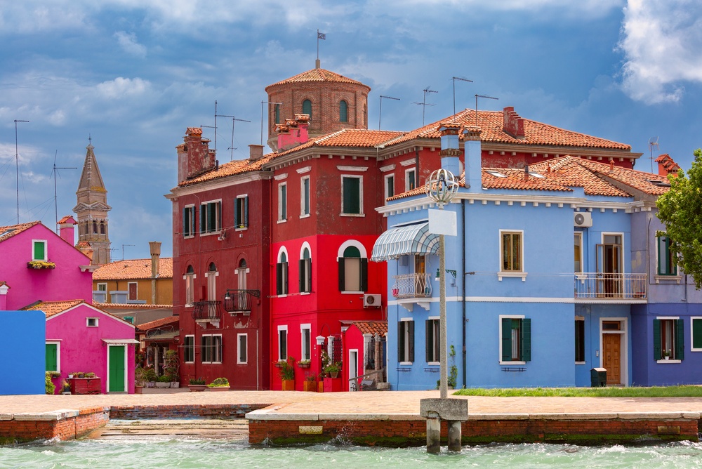 Colourful houses along a canal on Burano with the church tower in the background