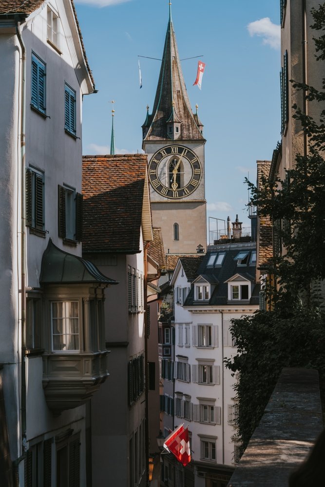 Street in Niederdorf in Zürich with Swiss flags and the tower of St. Peter in the background